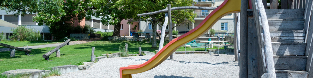 Spielplatz des Schulhauses mit Rutsche, Schaukeln und Wippe